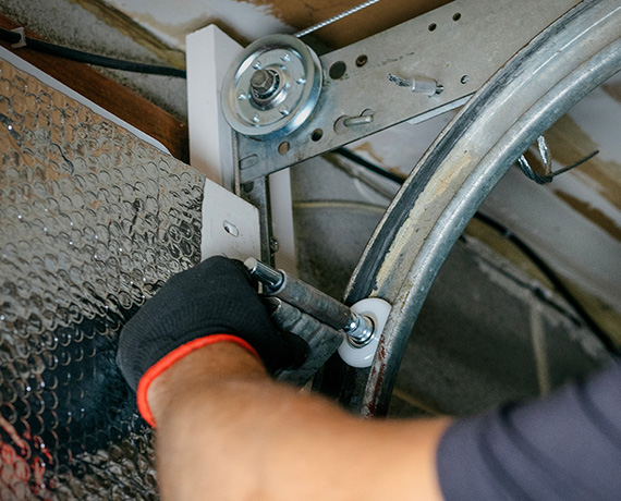 person using a wrench to adjust a garage door mechanism demonstrates essential home maintenance tools for homeowners in a safe environment