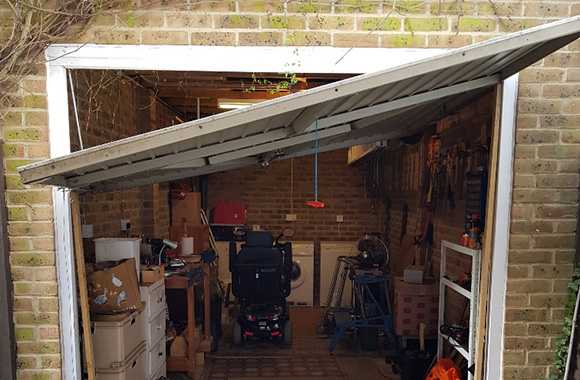 a partially open garage door revealing tools and equipment inside showcasing an untidy workspace with a mobility scooter inside the garage associated with seven home improvement projects