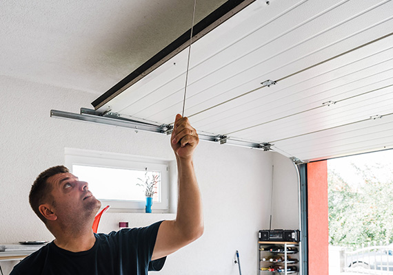 man pulling garage door mechanism in residential garage space with tools and a window visible showing a plant creativity six ways to improve garage