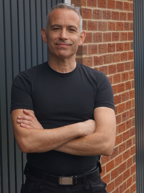 man with crossed arms in a black shirt standing against a brick wall showcasing strength and confidence in life changes and personal growth 5 ways to improve happiness