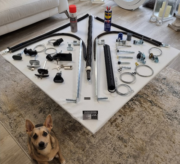 A collection of various tools and equipment arranged on a white surface with a dog in the foreground, showcasing parts for a project related to home improvement or repair featuring four essential items.